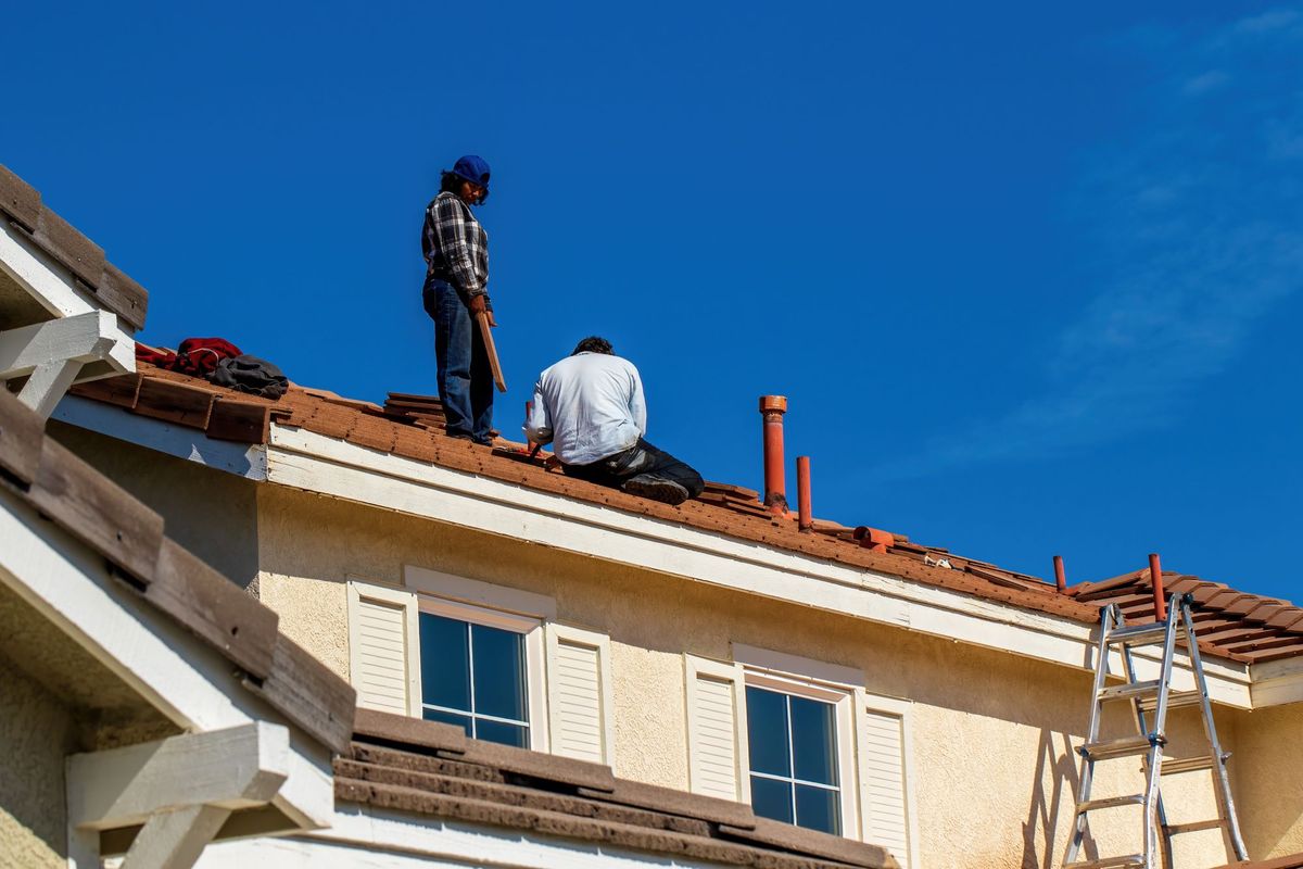Two roofers working on a damaged roof under a clear blue sky