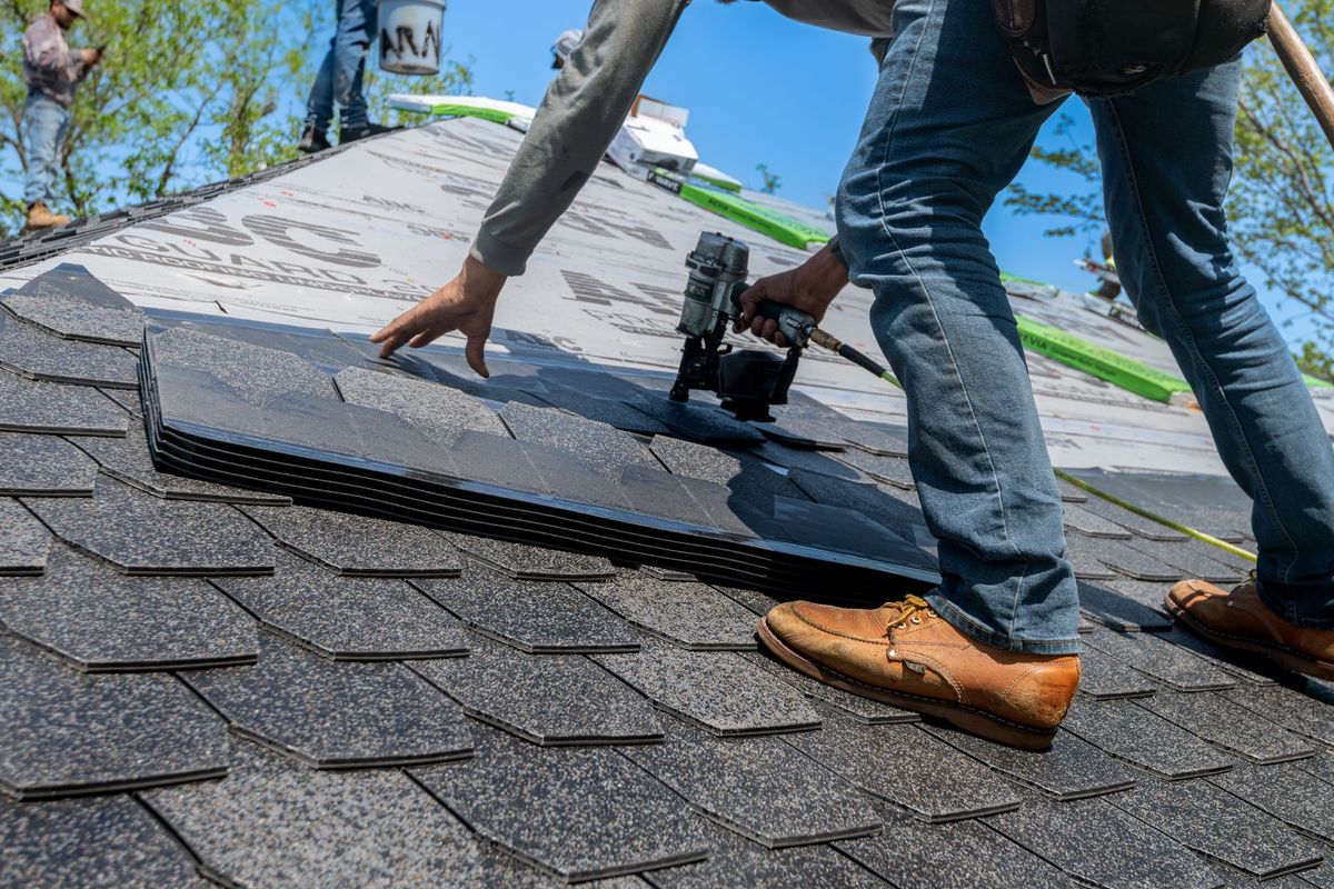 A roofer fastening new architectural shingles with a nail gun